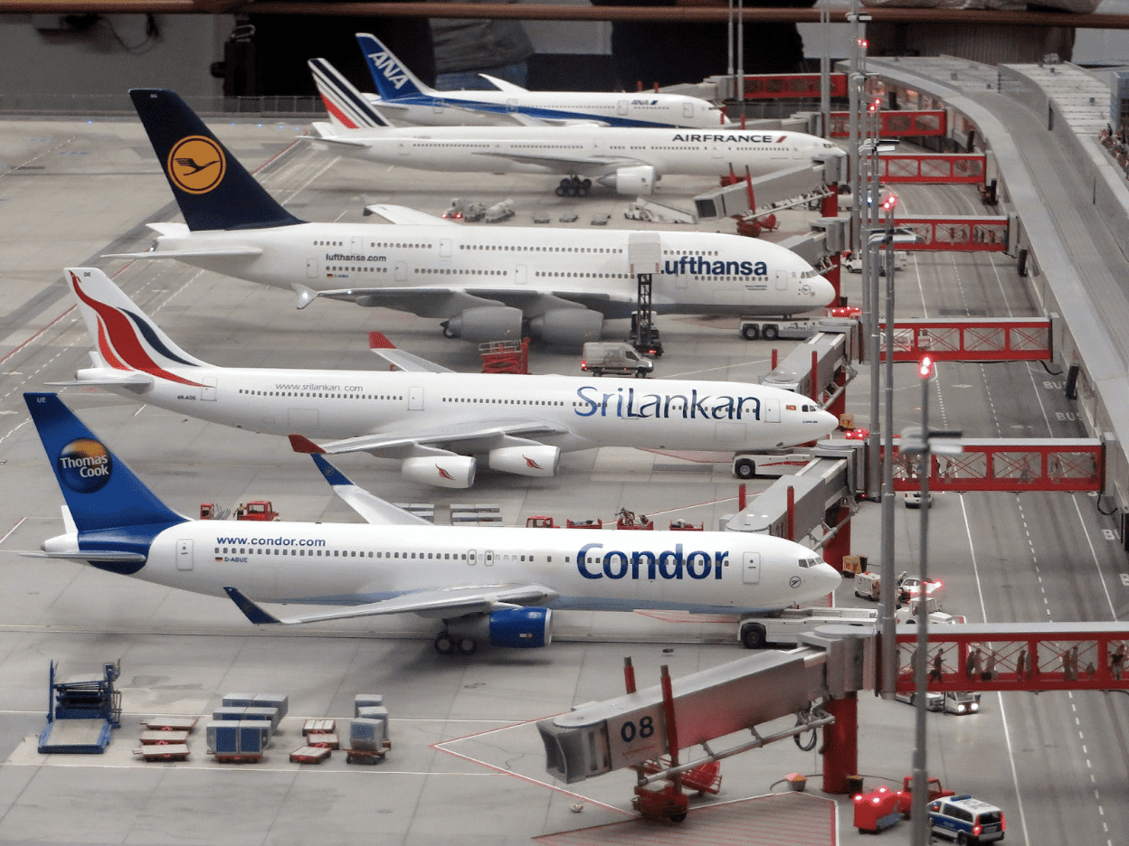 Line of aeroplanes from various airlines are parked at gates.