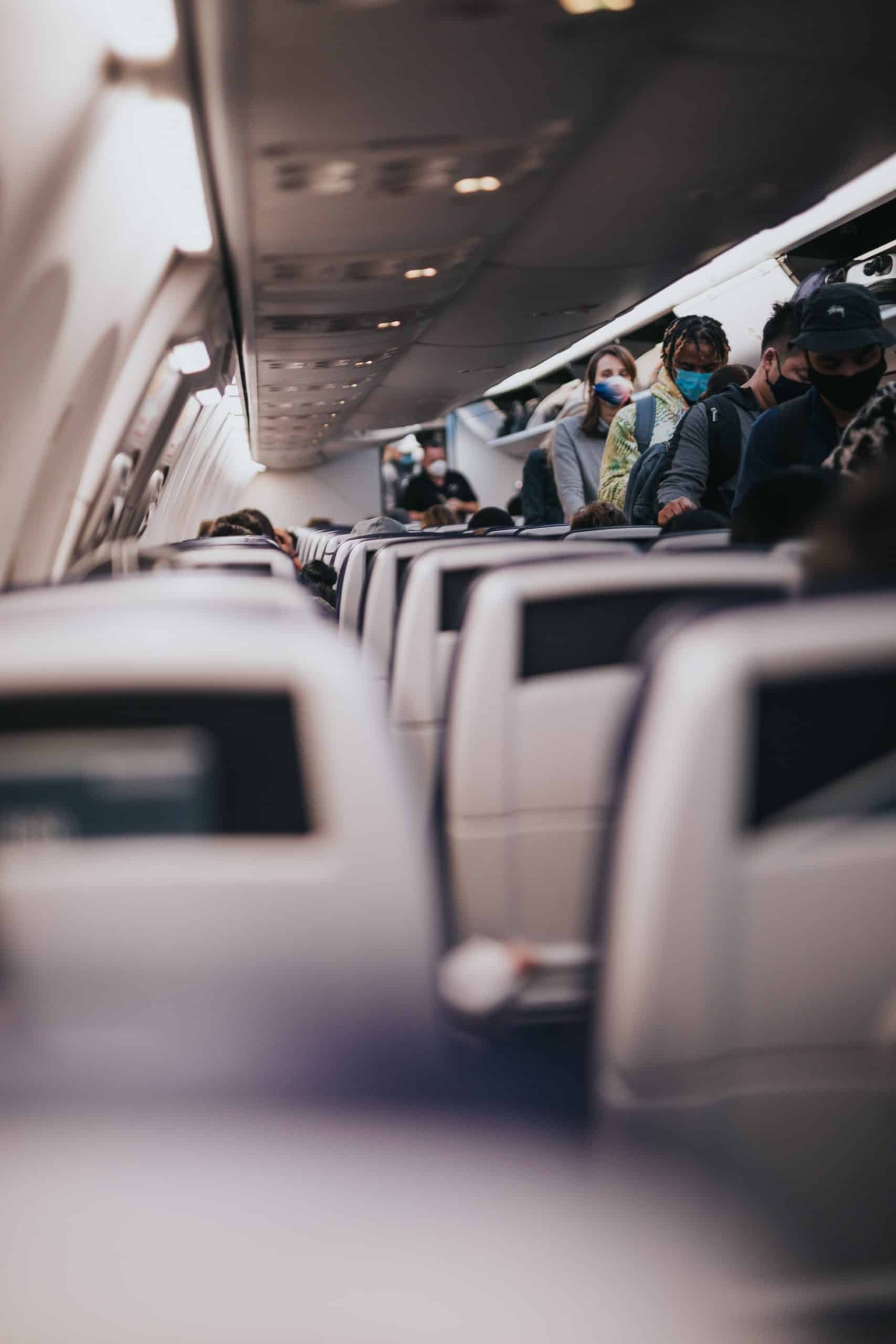 Interior shot of a plane, with passengers lined up to exit