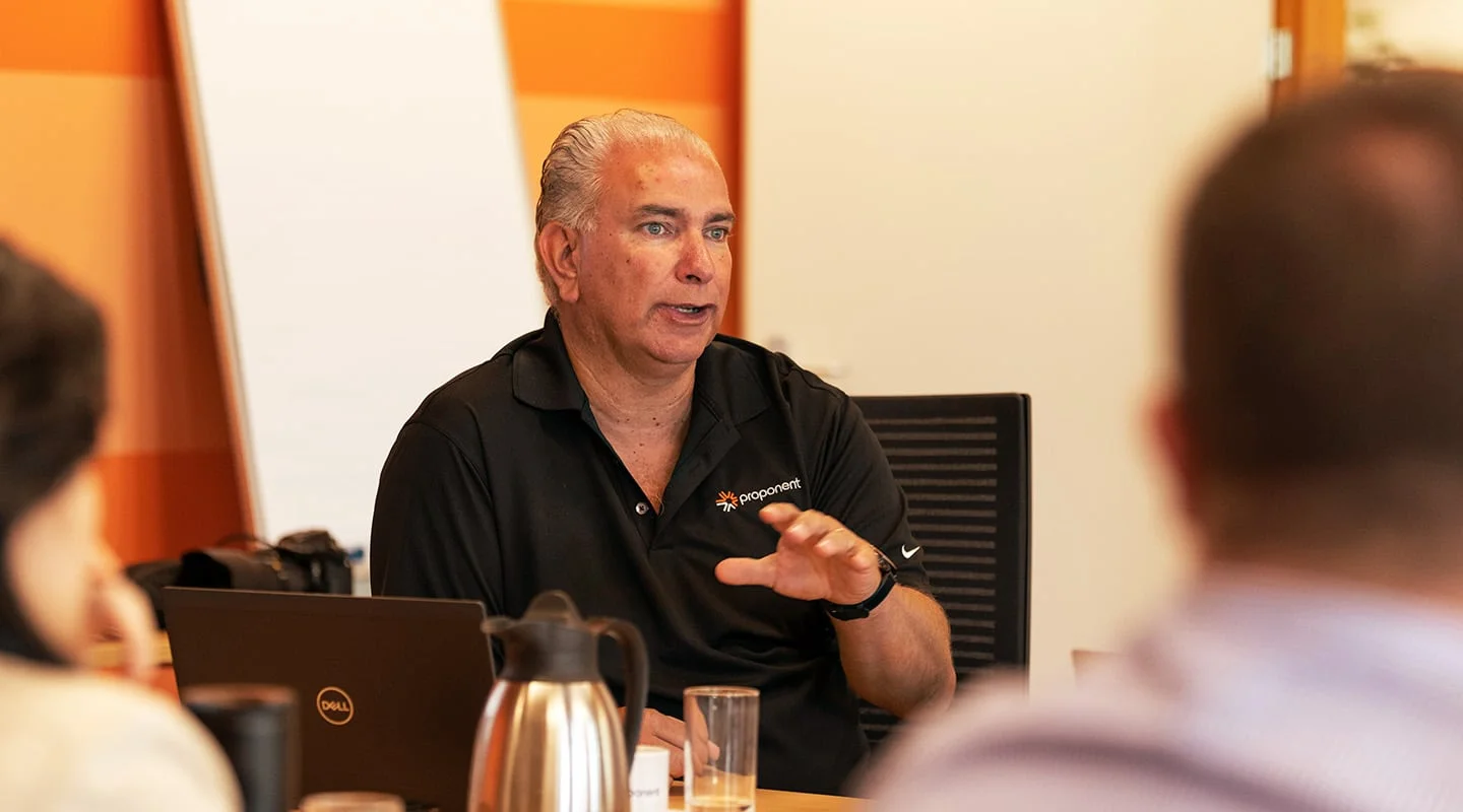 A man wearing a black Proponent branded shirt, talks to a group