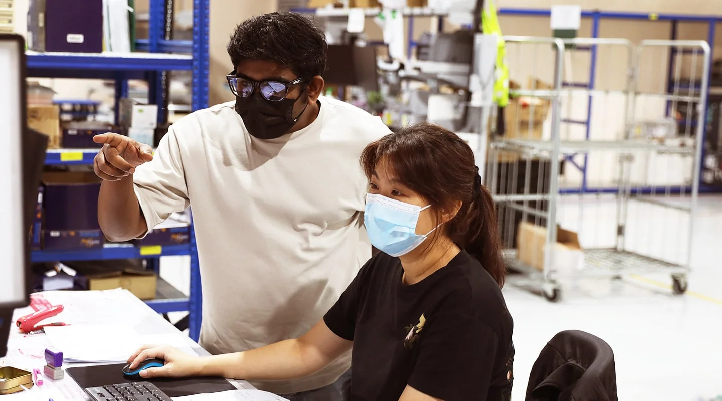 Two people work at a computer wearing masks in Singapore
