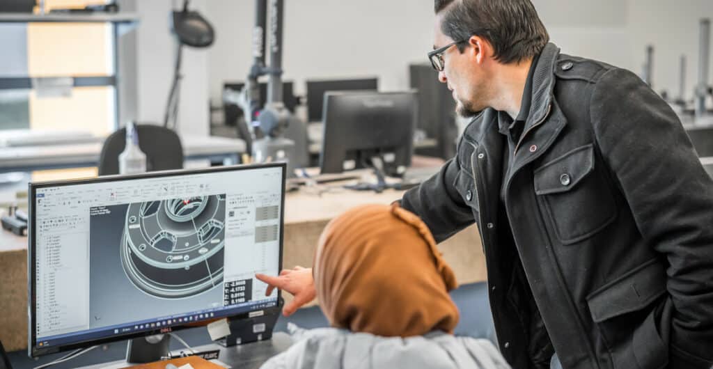 Two employees work at a computer, showing CAD