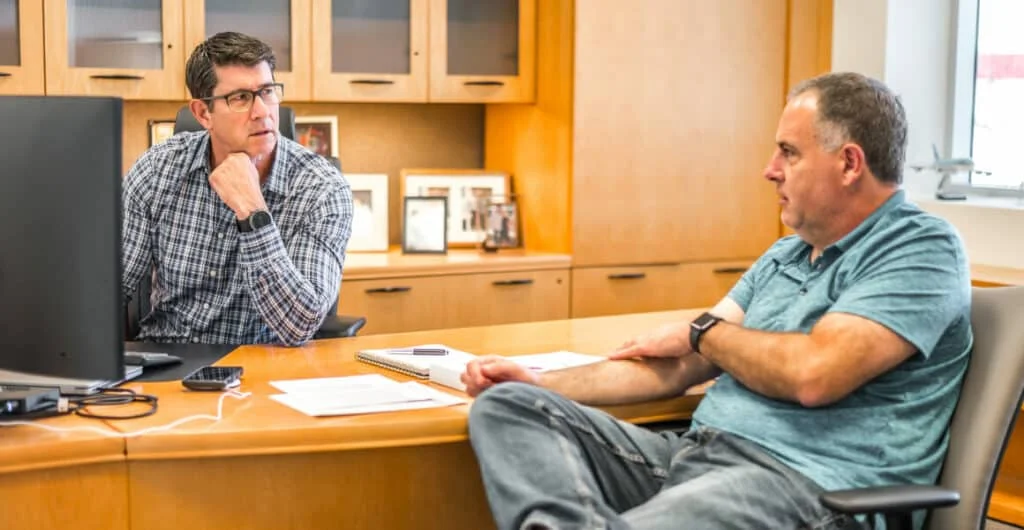 Two men talking on opposite sides of a desk
