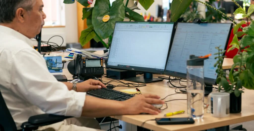 An employee works at a computer, with plants around him