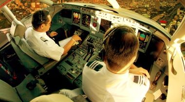 Two pilots in a cockpit, flying over a city