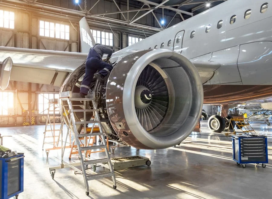 A man performs maintenance on a jet engine in a hangar.