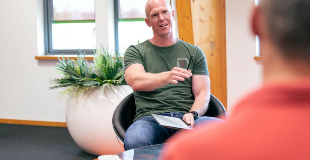 A man in a green shirt, talks to person in a salmon shirt