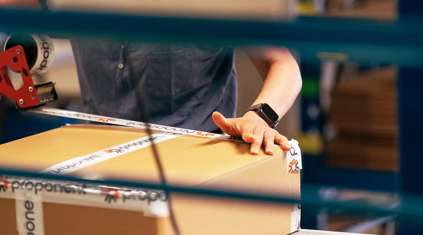 An employee taping a box shut for shipping, with Proponent branded tape