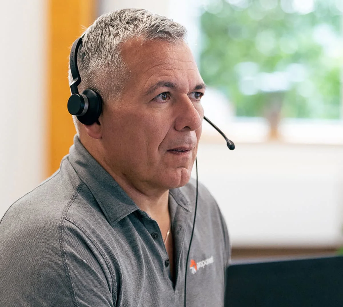 A man in a grey Proponent branded shirt, wearing a headset
