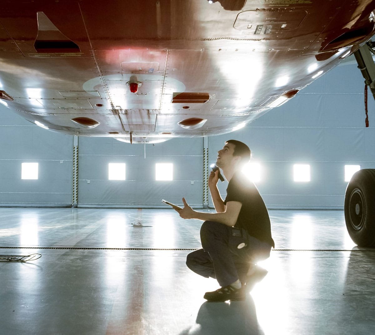 A man inspects the underside of a plane, in a hangar