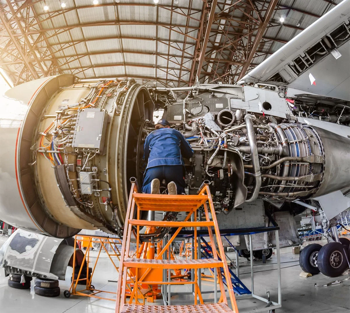 Medium shot of a mechanic working on a jet engine, in a hanger.
