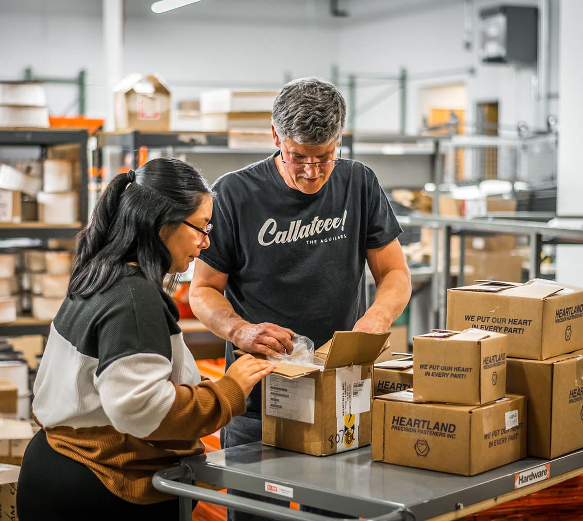 Two employees look inside a cardboard box, in a warehouse