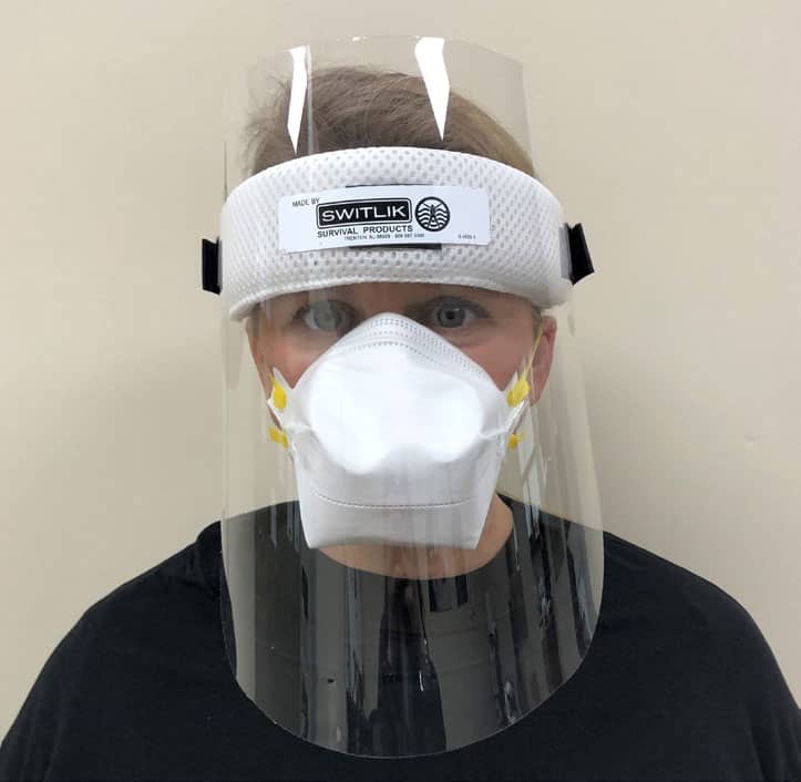 A model in a black shirt, wearing a facemask and plastic face shield