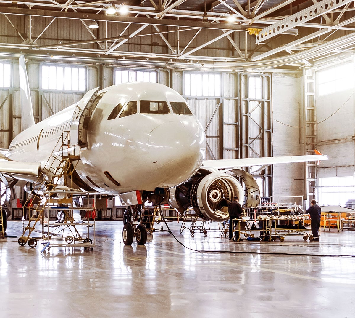 White jet engine plane, being working on in a hanger by two mechanics.