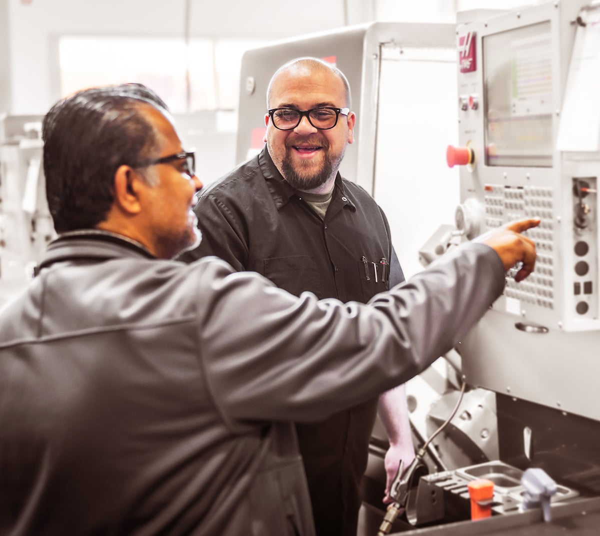 Two men, in mid conversation, working at a control panel.