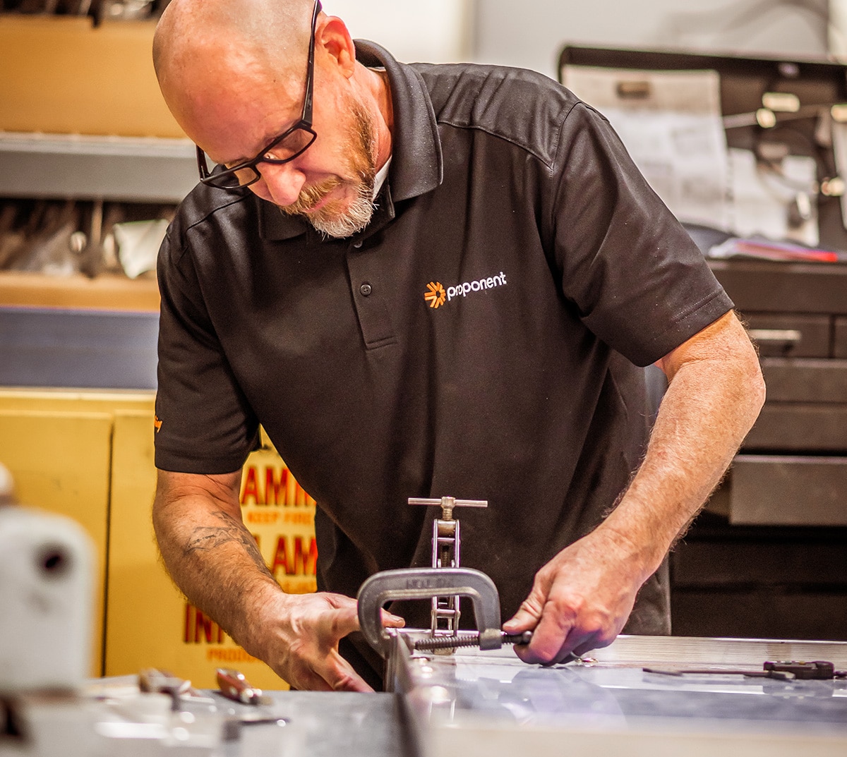 Closeup of a man clamping down a part, wearing a black Proponent branded shirt.