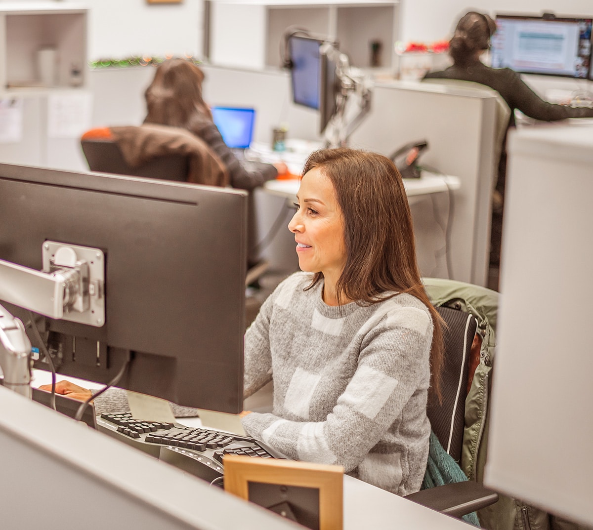 Medium shot of a team working at computers, with a woman in the foreground wearing a grey and white jumper.