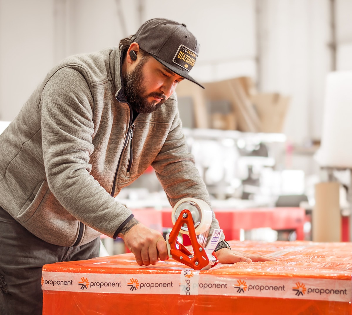 A man in a grey jumper and hat, tapes a box for shipping